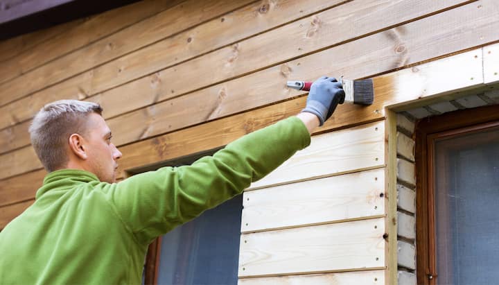 A professional painter using a long-handled brush to apply paint to the exterior of a house in Bend.